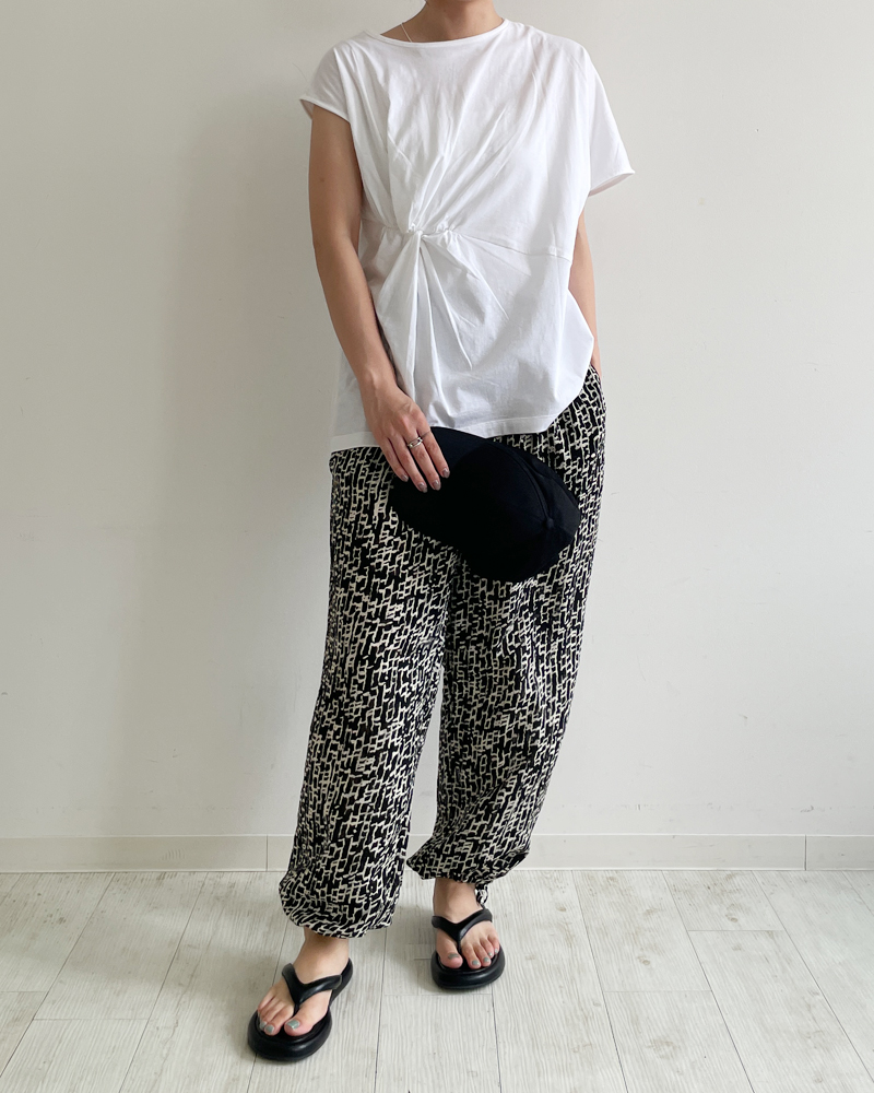 30代・40代・50代女性向け、夏のBBQに最適な大人のカジュアルファッション。白のねじりデザインTシャツに黒白柄パンツ、黒キャップと厚底サンダルを合わせた動きやすくて涼しいアウトドアコーデ。
