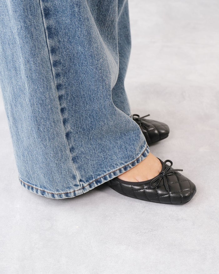 ワイドデニムパンツの裾から覗く、フロントにリボンをあしらったブラックのキルティングバレエシューズの着用足元拡大画像。
