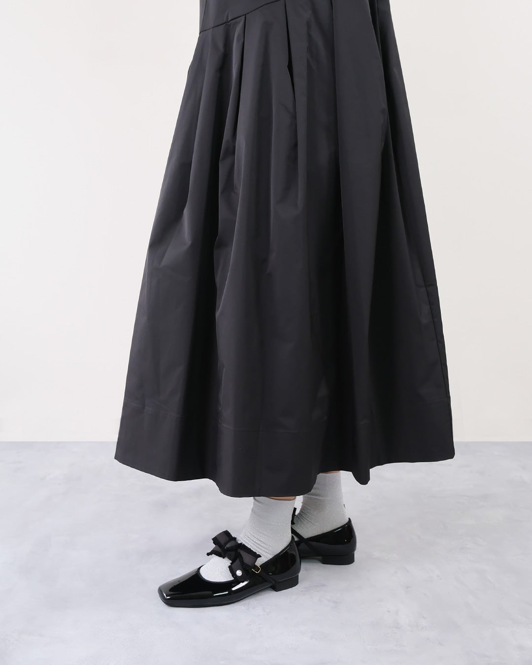 黒のフレアフレアスカートとシルバーソックスにリボン付きブラックエナメルストラップパンプスを合わせた下半身側面アングル。